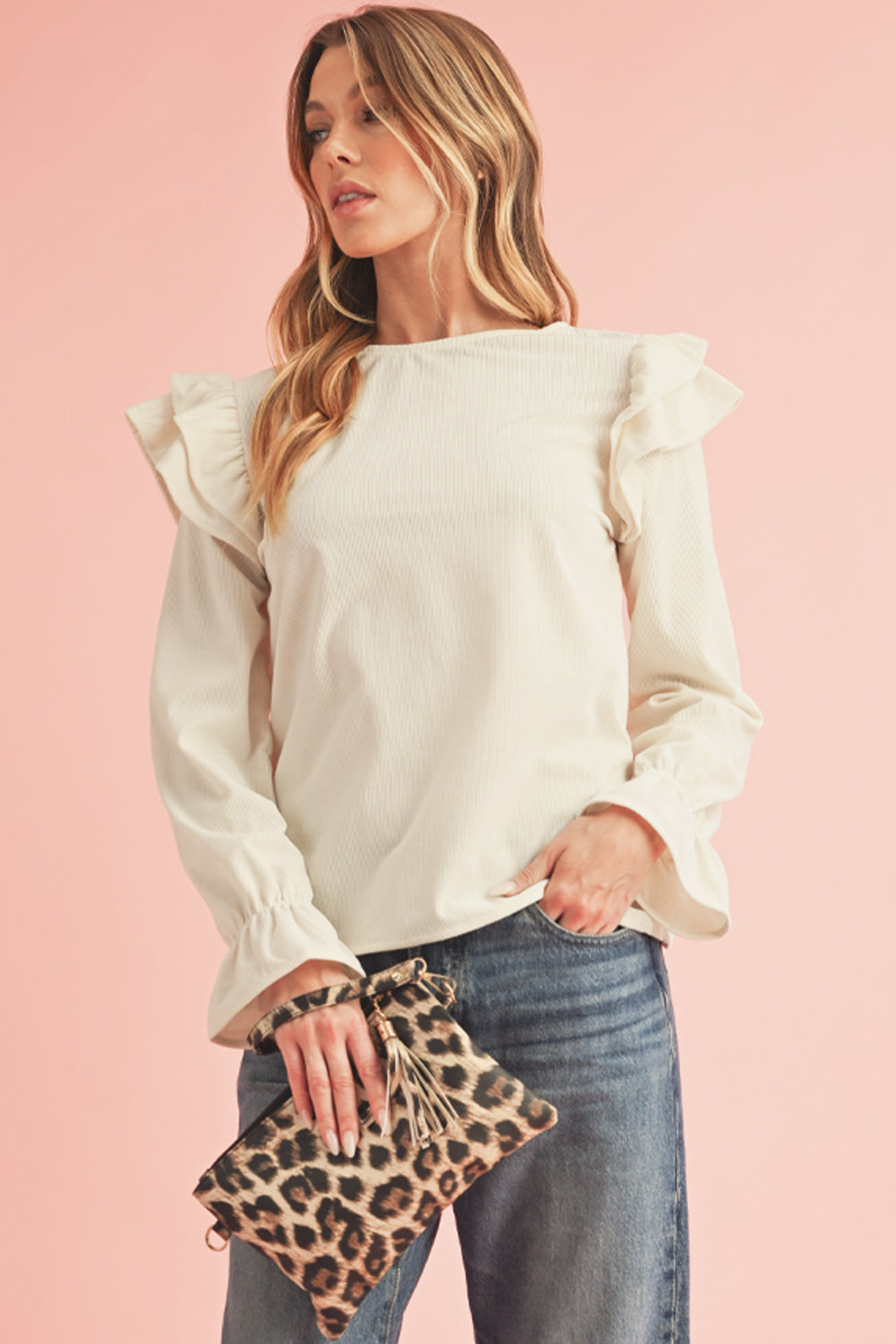 Woman wearing a white blouse with ruffled sleeves and holding a leopard print clutch against a pink background