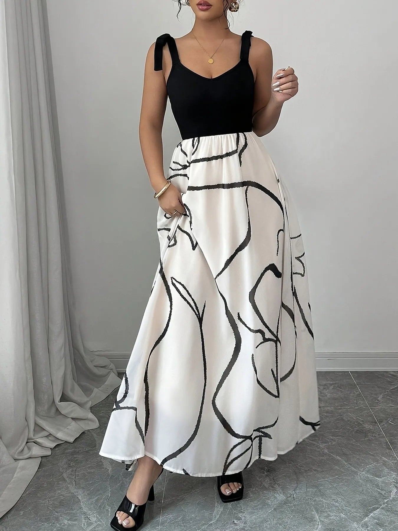 Woman wearing a black top and white skirt with black abstract patterns against a gray curtain background.