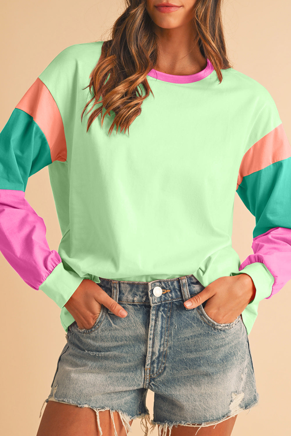 Person wearing a colorful long-sleeve top with pink, green, and red sleeves on a beige background