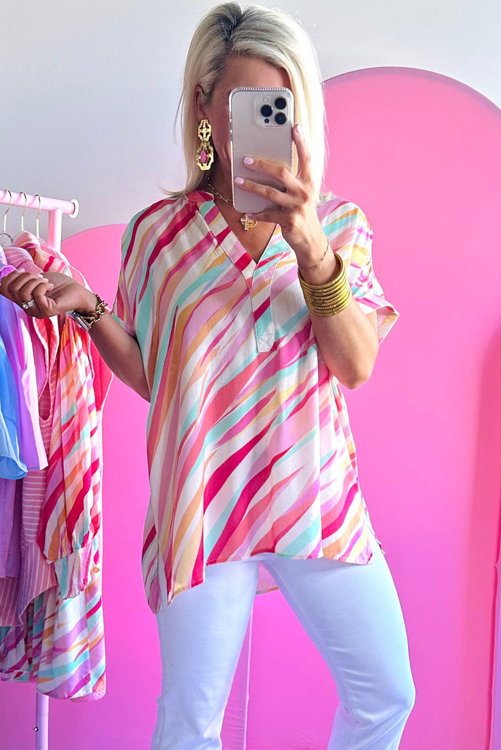 Person wearing a colorful striped shirt taking a mirror selfie in a pink room.