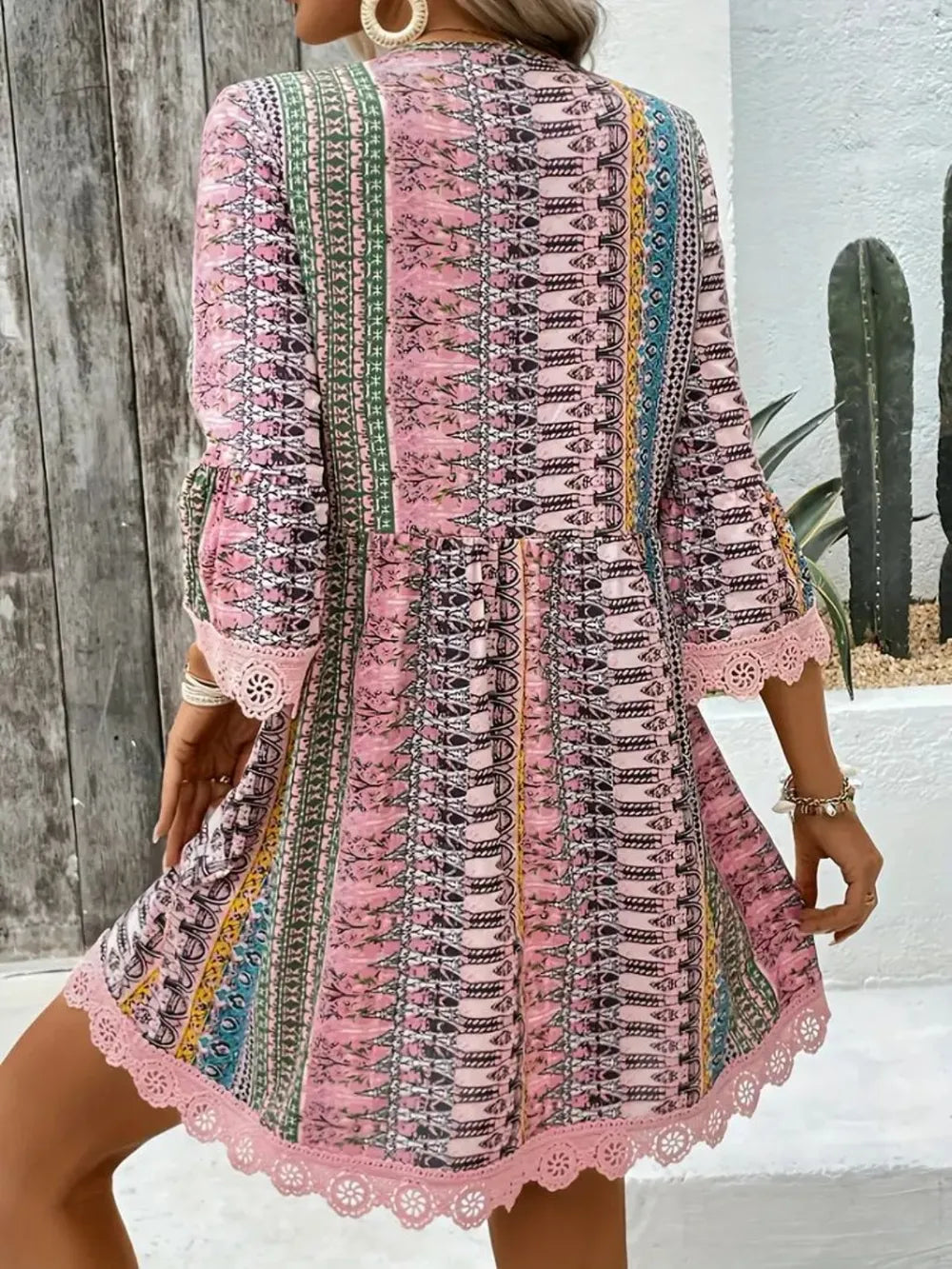 Woman wearing a colorful patterned dress with long sleeves in an outdoor setting.