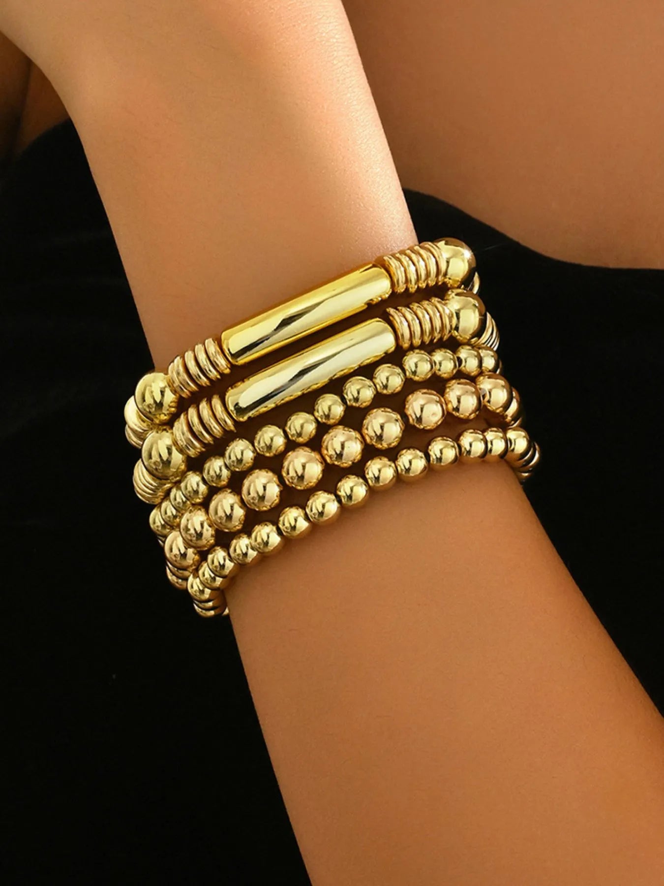 Gold beaded bracelet on a wrist against a black background