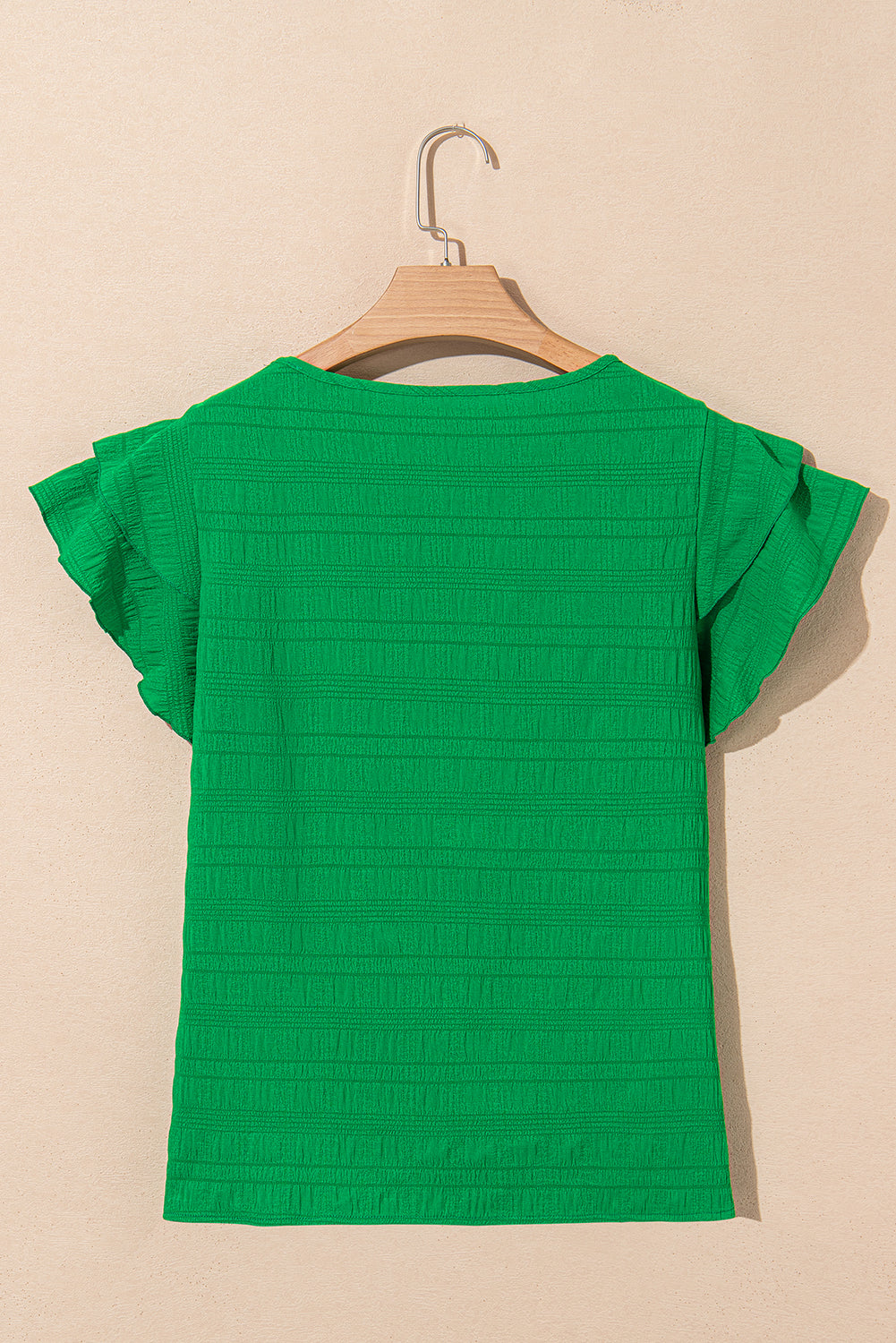Green textured top on a wooden hanger against a beige background