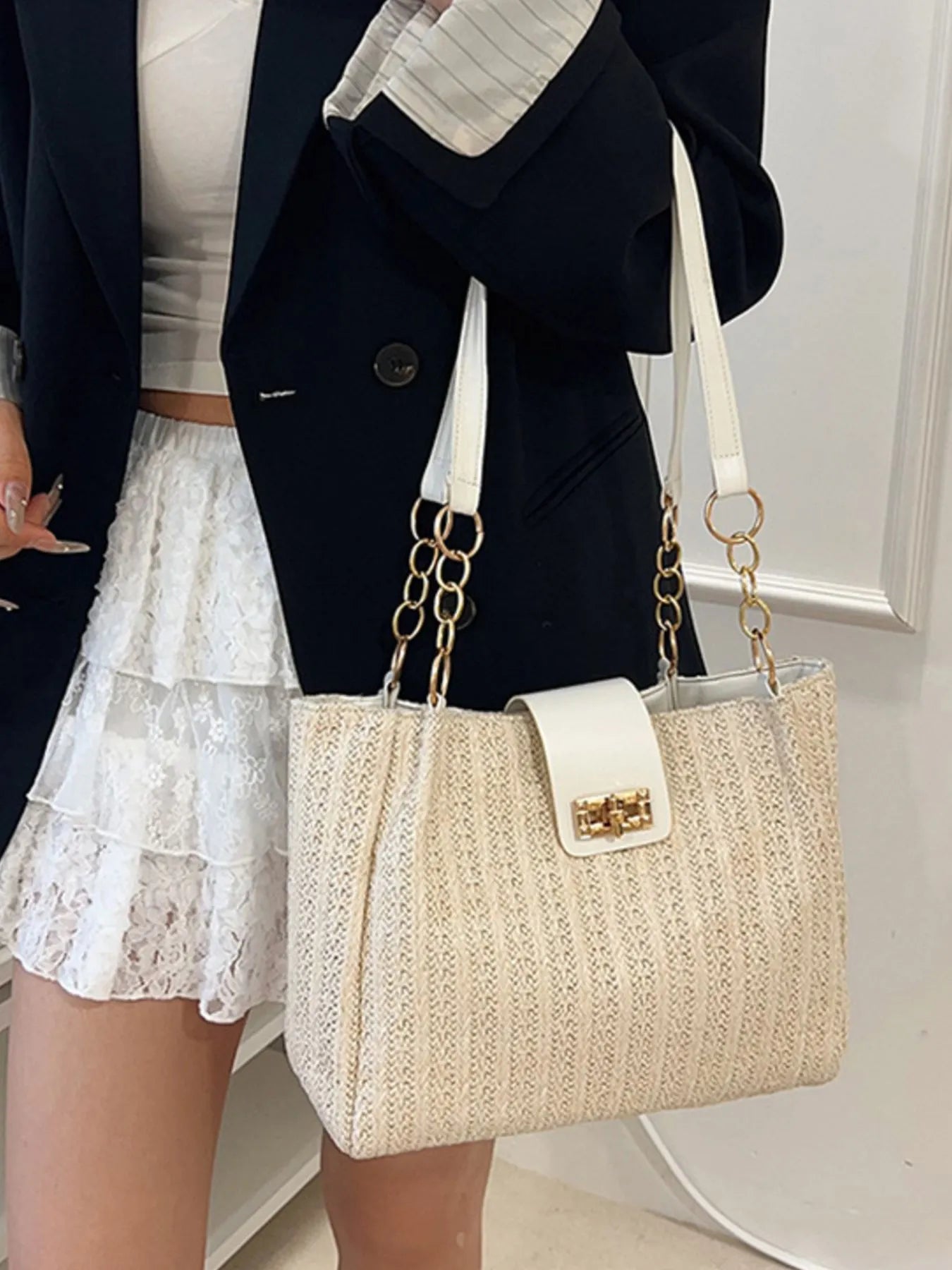 Person wearing a black blazer and white lace skirt with a beige handbag.