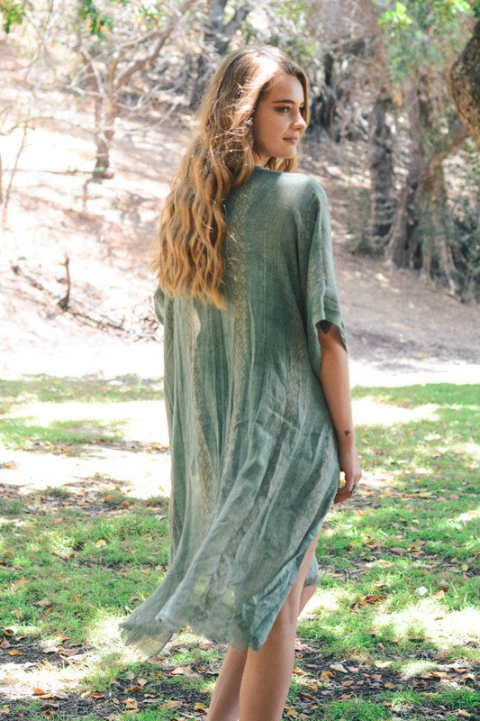 Woman wearing a green dress standing in a natural setting with trees and grass.