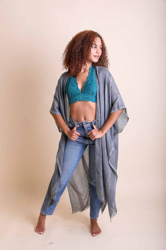 Woman wearing a teal crop top and blue jeans with a gray draped garment on a beige background