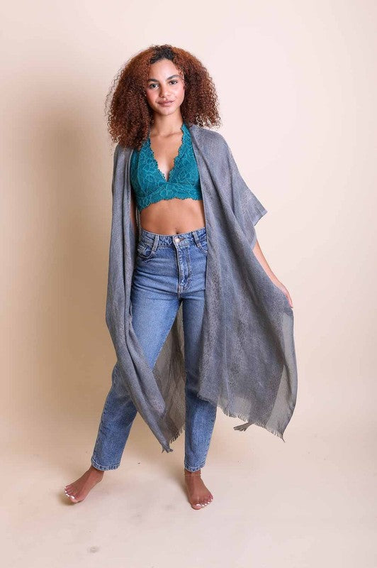Woman wearing a teal crop top and blue jeans with a gray scarf on a beige background