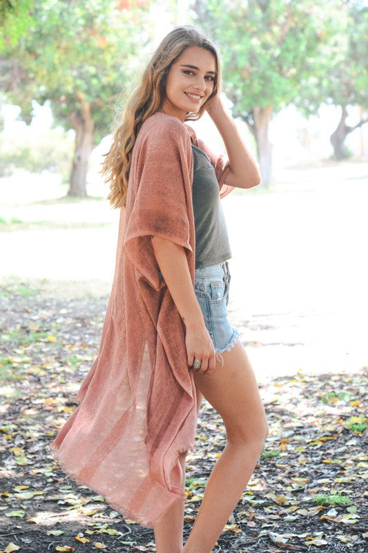 Woman wearing a pink kimono-style garment in an outdoor setting with trees and ground cover.