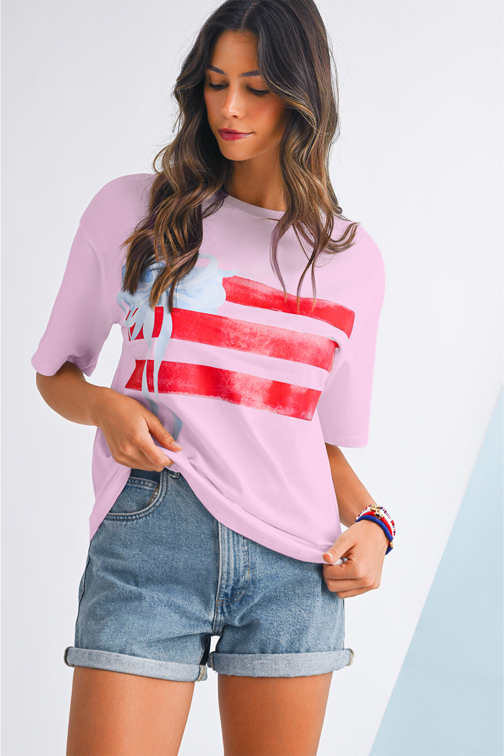 Woman wearing a pink t-shirt with red and blue design and denim shorts on a light gray background