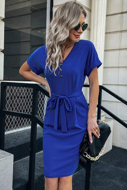 Woman wearing a blue dress with a belt, standing on steps outside a building.