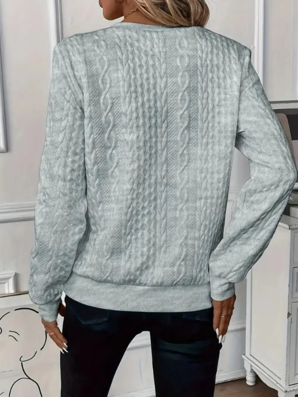 Person wearing a light blue cable knit sweater in an indoor setting.