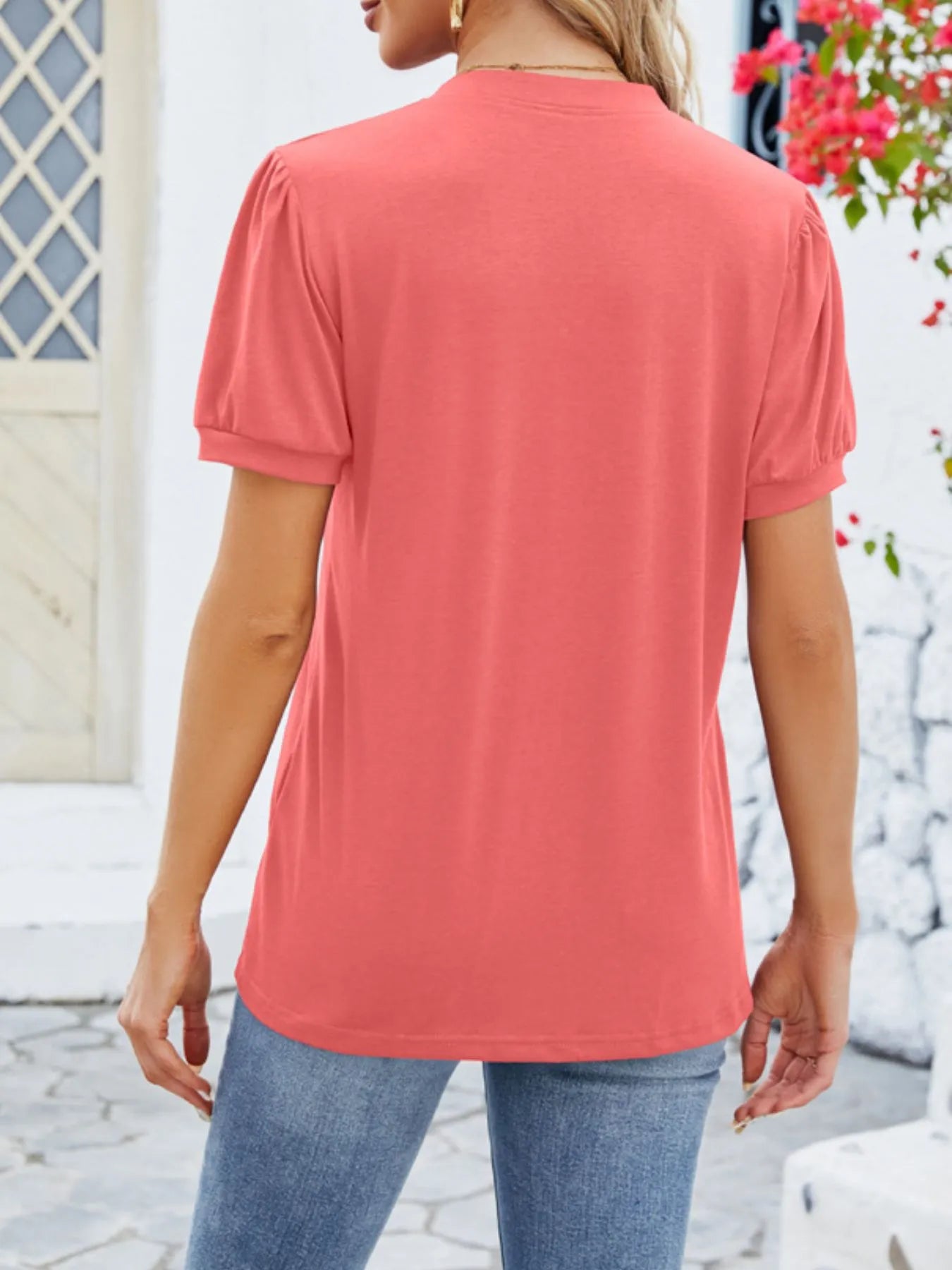 Person wearing a coral t-shirt and blue jeans standing outdoors with a blurred background