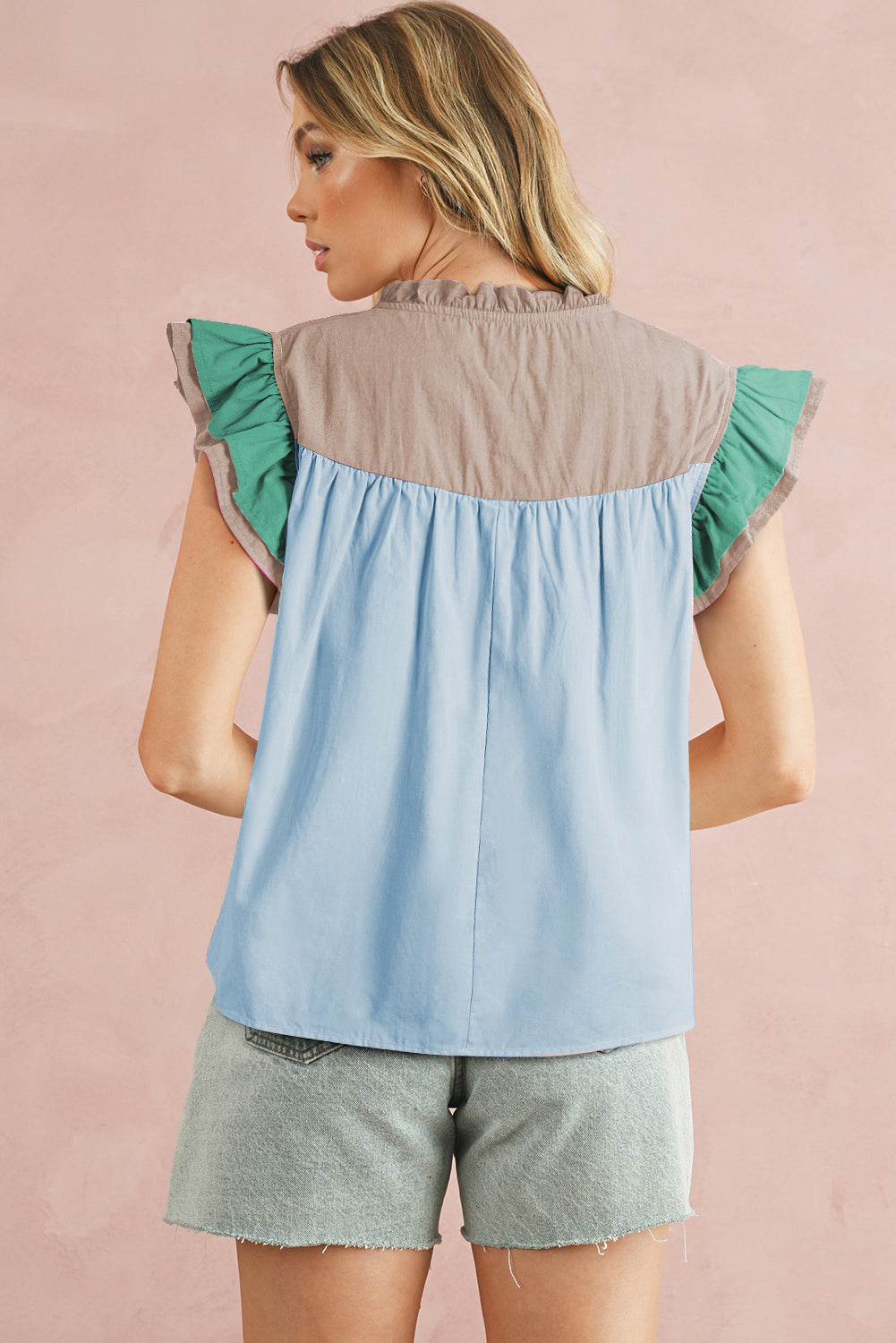 Woman wearing a two-tone top with green and blue sleeves on a pink background