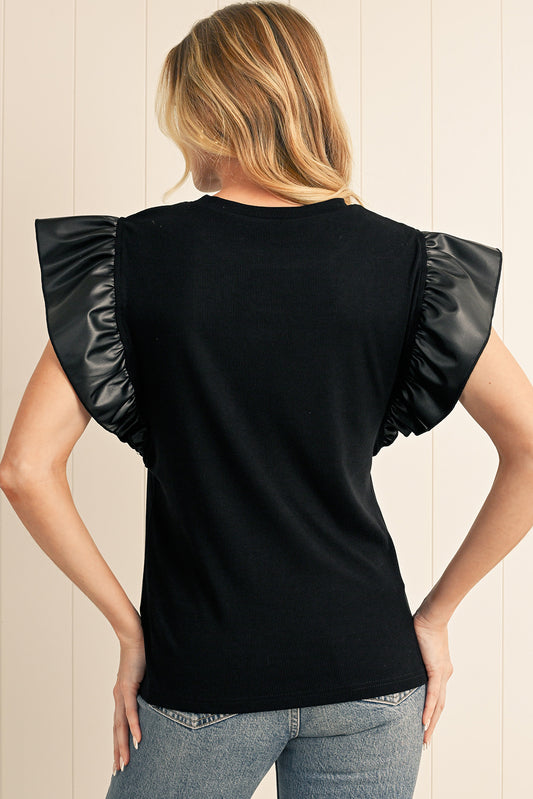 Woman wearing a black top with ruffled sleeves against a beige wall.