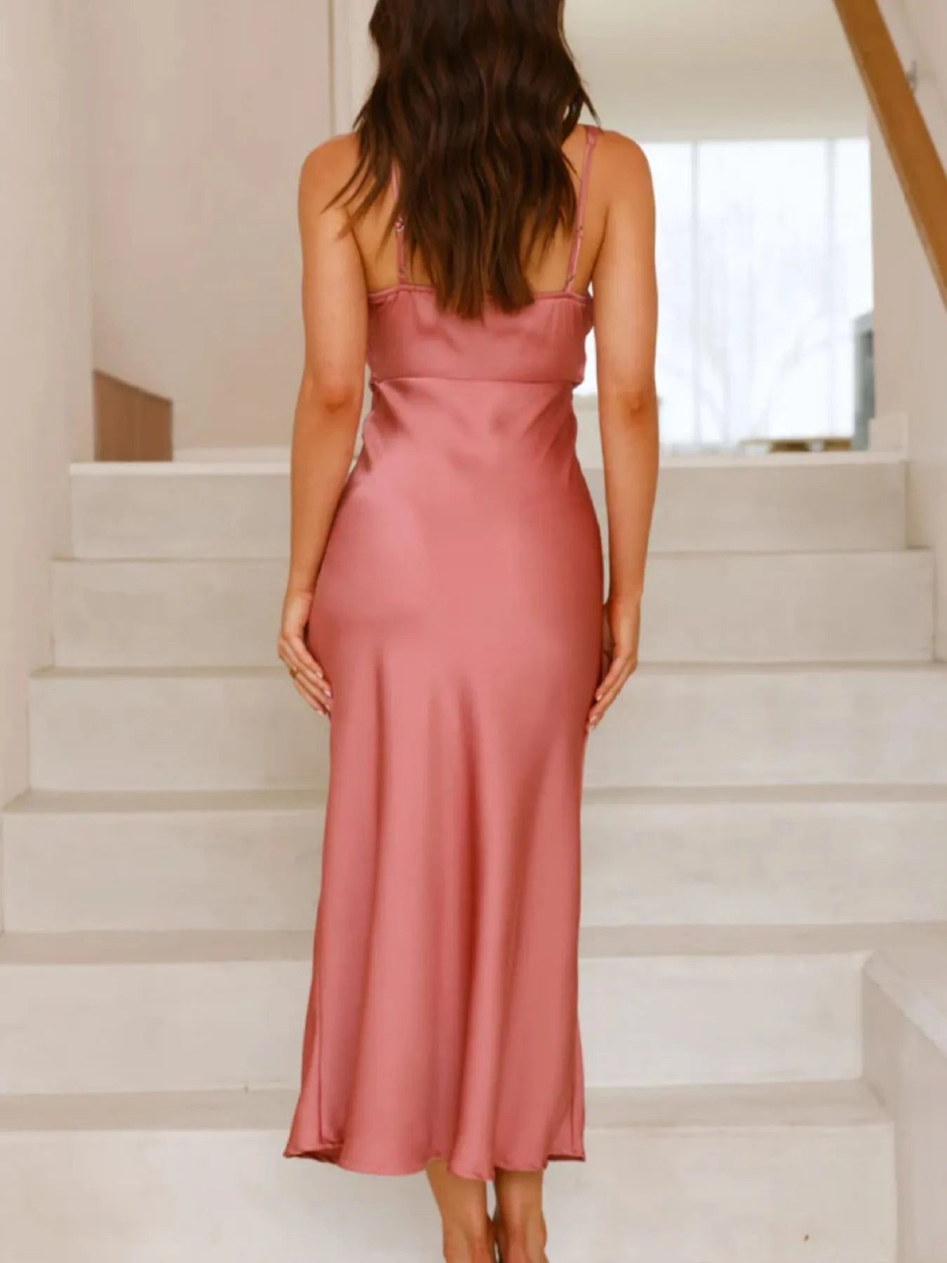 Woman wearing a pink satin dress standing on a staircase.