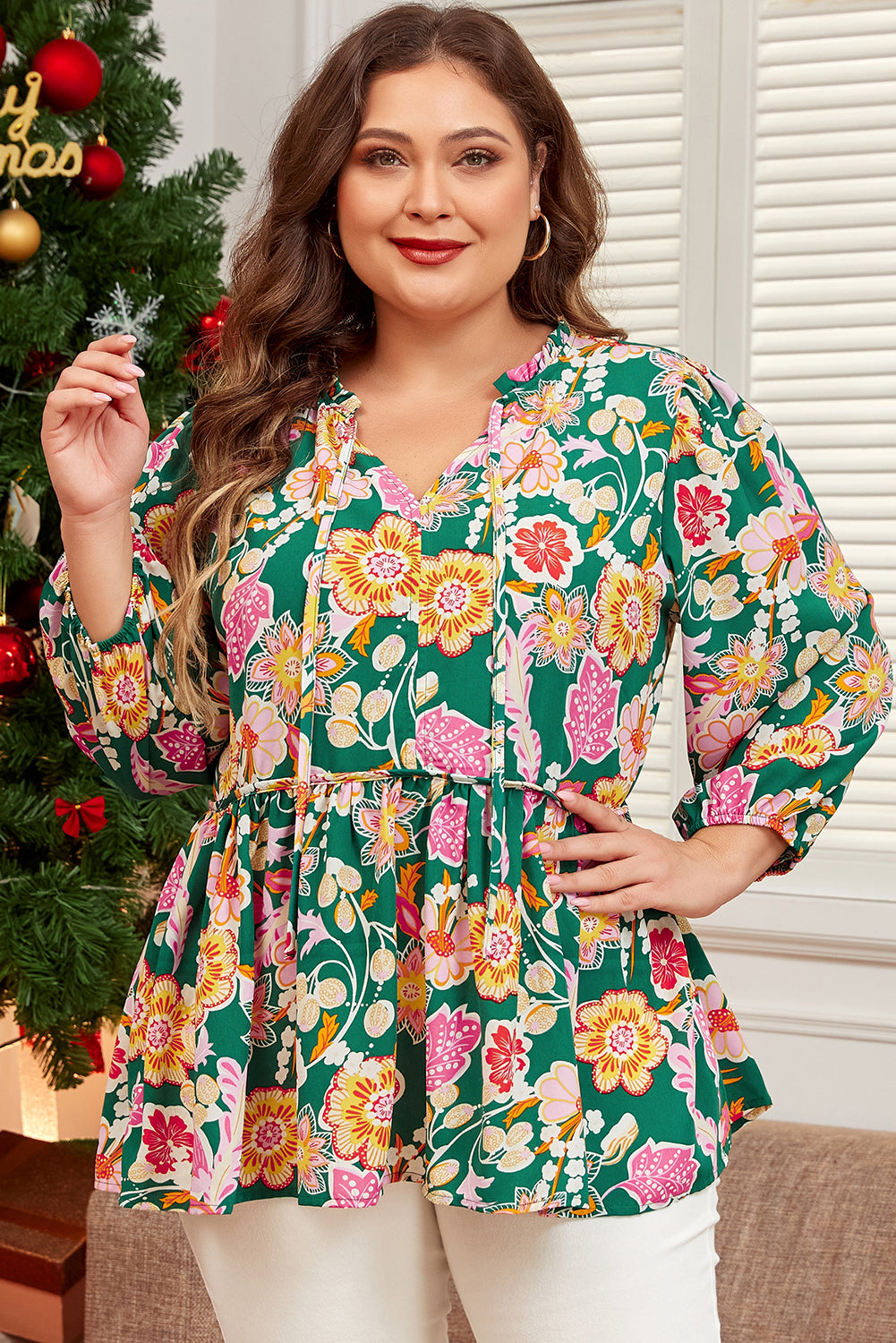 Woman wearing a floral blouse in front of a decorated Christmas tree
