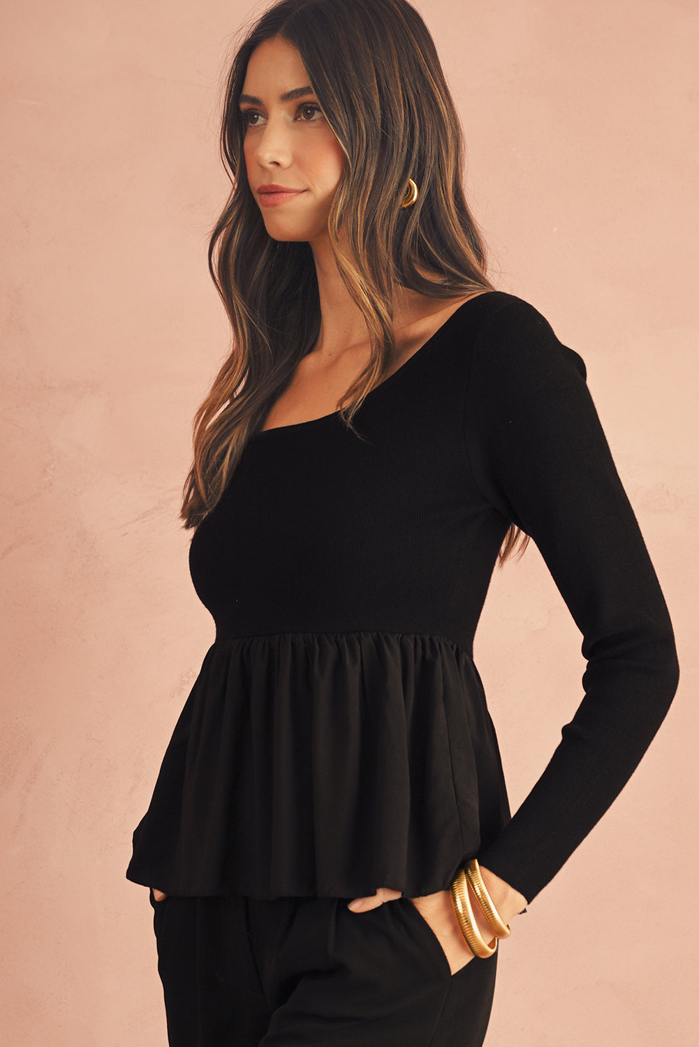 Woman wearing a black peplum top against a beige background