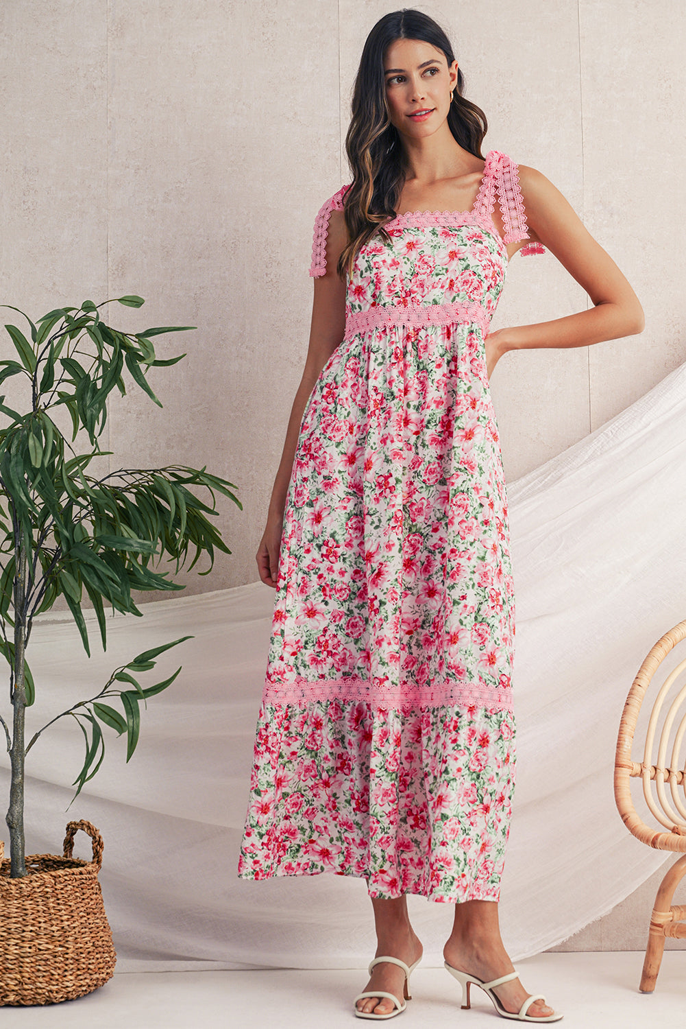 Woman wearing a floral dress standing indoors with a plant and chair in the background