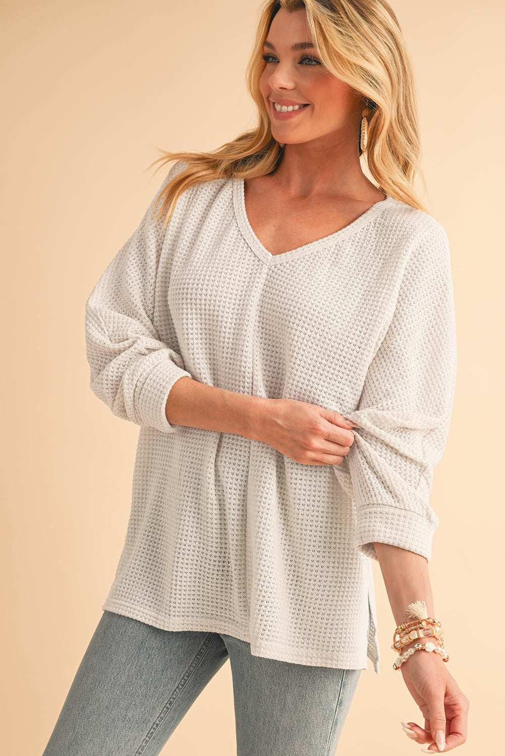 Woman wearing a light gray textured sweater and jeans on a beige background