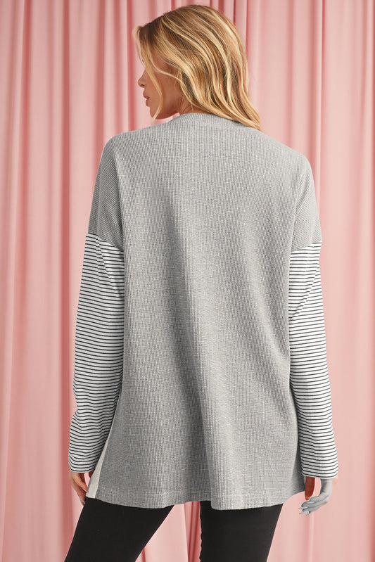 Person wearing a gray sweater with striped sleeves against a pink curtain background