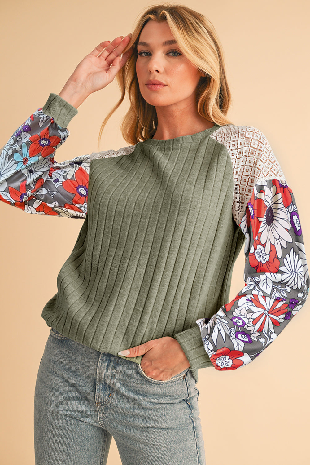 Woman wearing a green ribbed sweater with colorful floral sleeves on a beige background