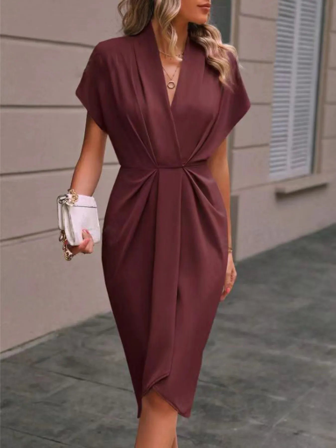 Woman wearing a burgundy dress holding a white clutch against a neutral background
