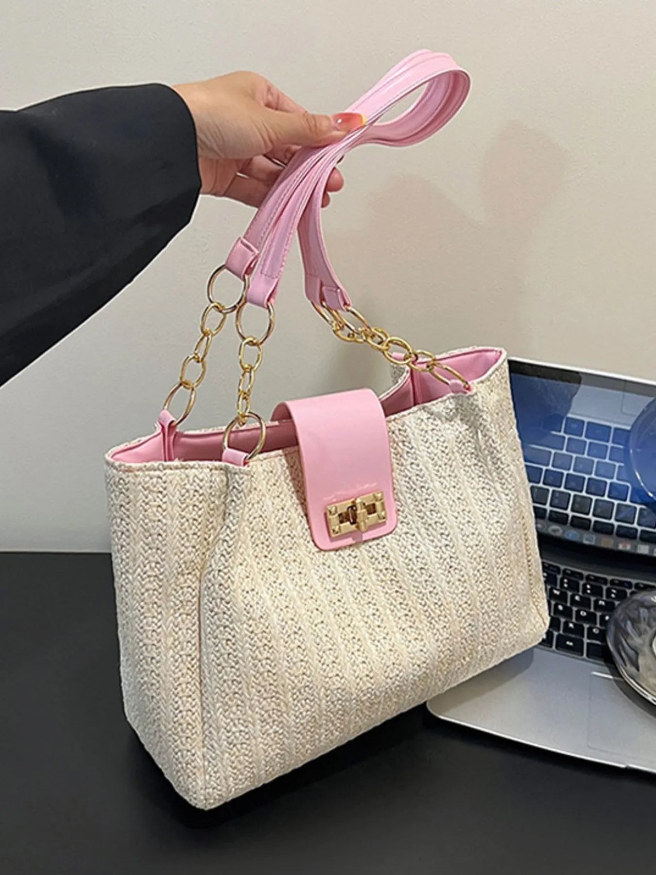 Handbag with pink handle and trim held by a person, with a laptop in the background.