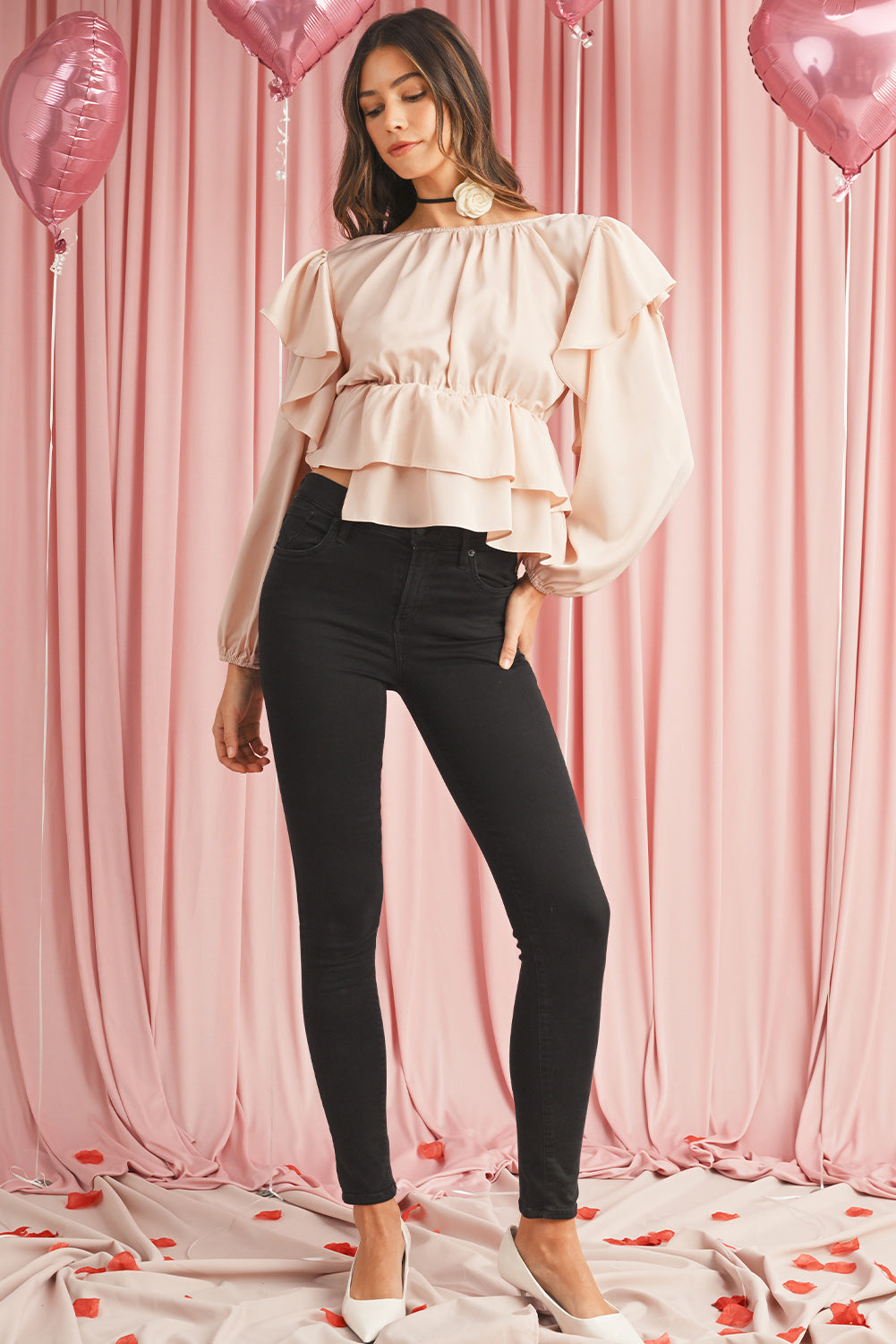 Woman wearing a light pink blouse and black pants against a pink curtain background with balloons.