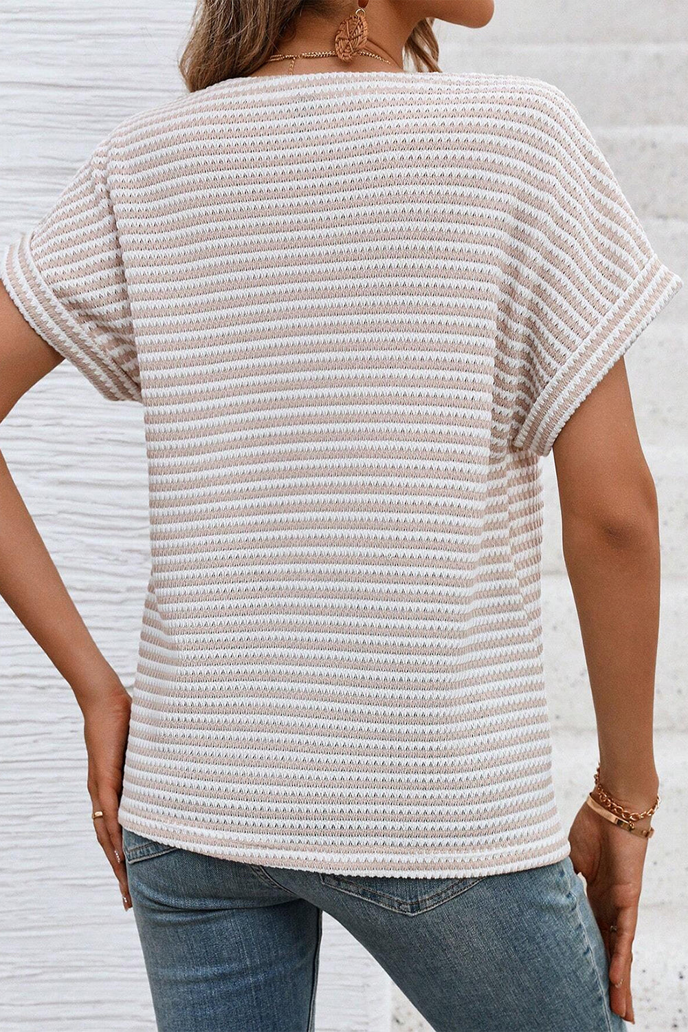Person wearing a textured white top and blue jeans against a light gray background