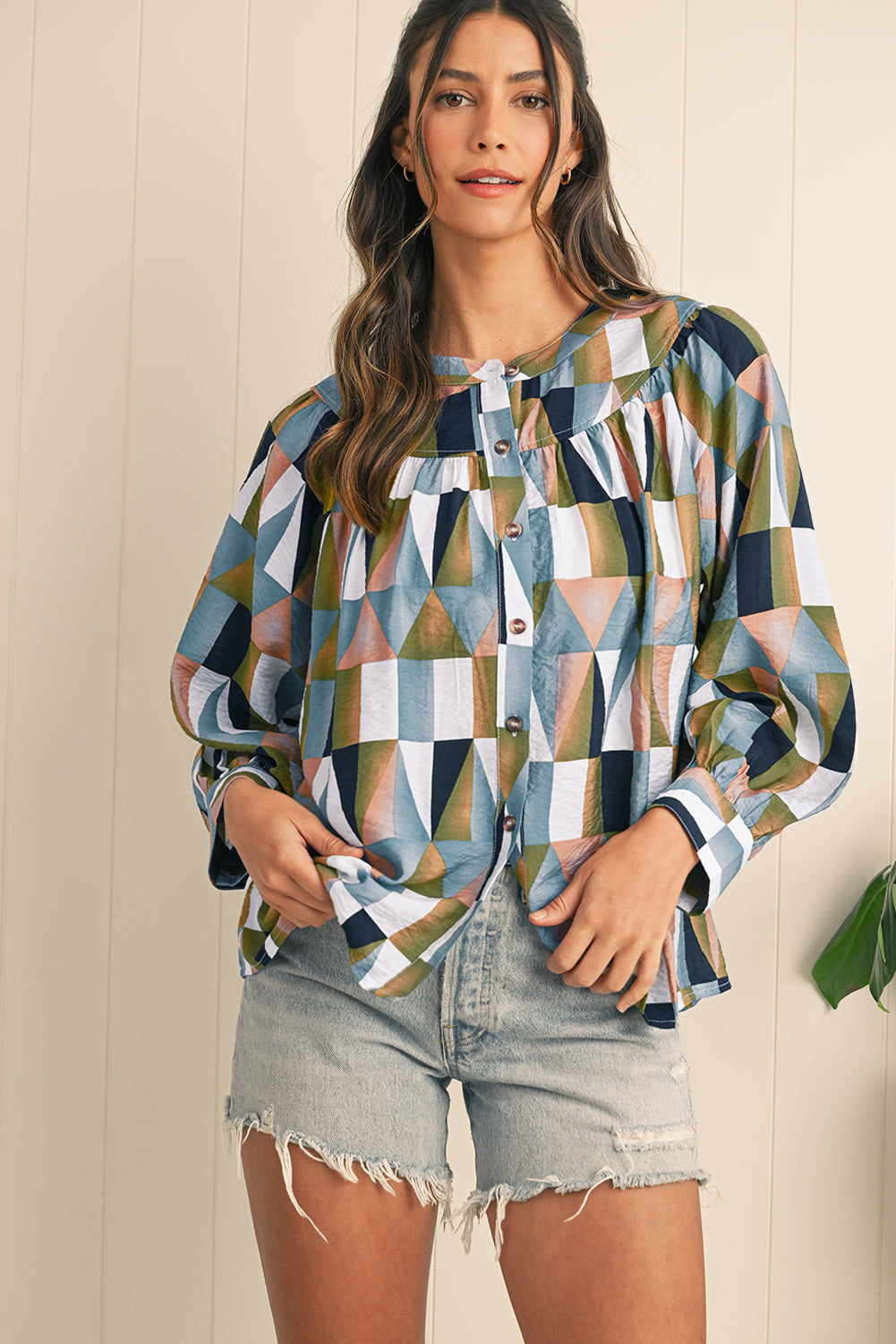 Woman wearing a colorful geometric patterned shirt and denim shorts against a neutral background