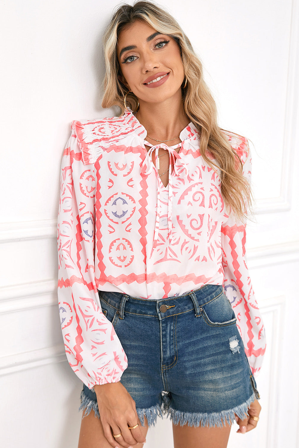 Woman wearing a pink and white patterned blouse with denim shorts against a white background