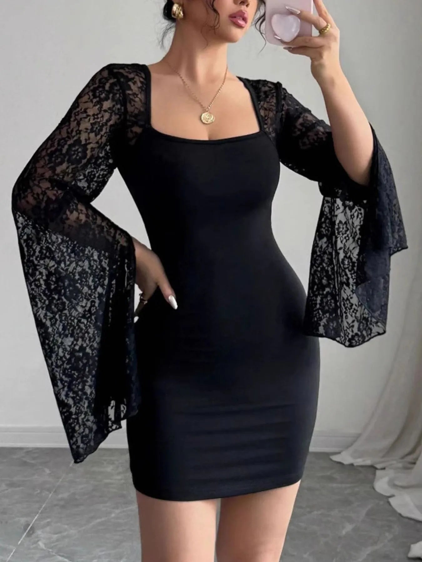 Person wearing a black dress with sheer lace sleeves against a neutral background