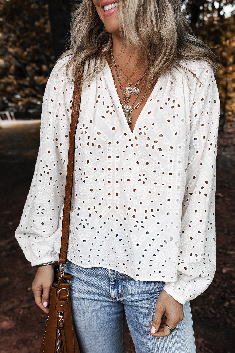 Woman wearing a white blouse with brown polka dots and blue jeans, standing outdoors.