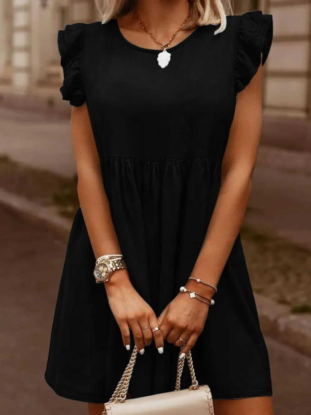 Woman wearing a black dress with ruffled sleeves, holding a cream handbag.