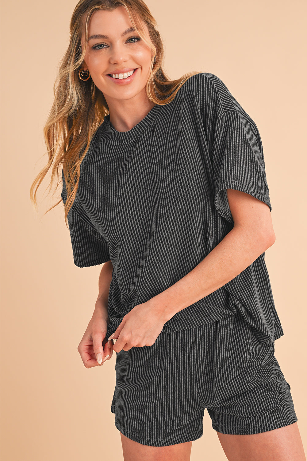Woman wearing a matching black and white striped top and shorts set on a beige background