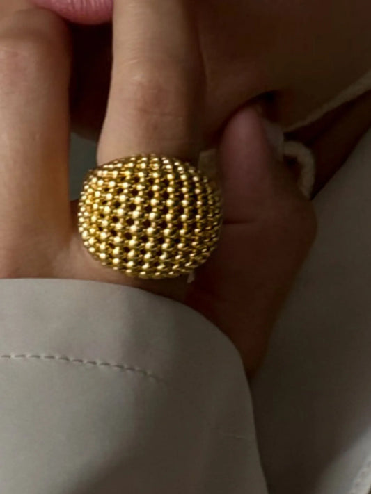 Gold beaded ring on a person's finger with a neutral background