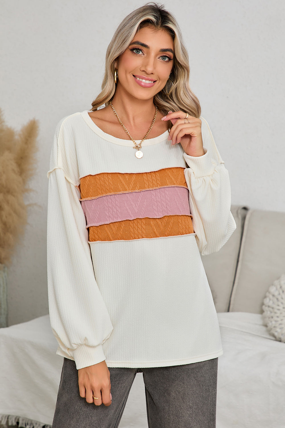 Woman wearing a white long-sleeve top with colorful stripes, standing in a room with a neutral background.