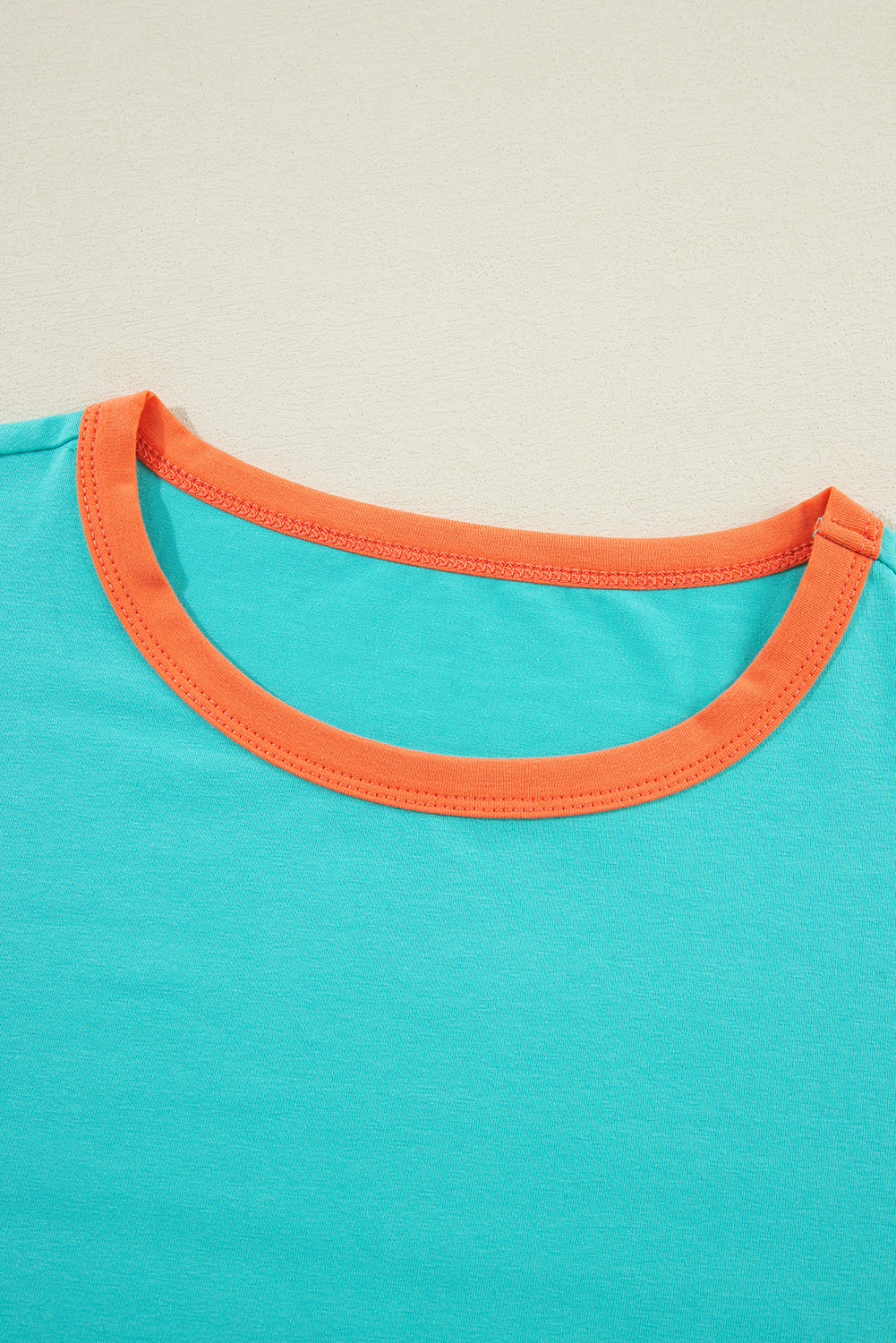 Close-up of a turquoise shirt with an orange neckline on a beige background