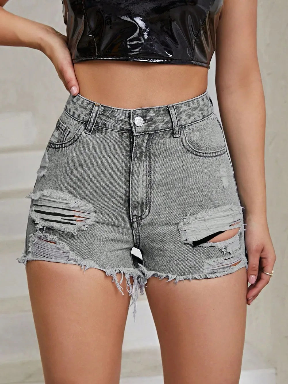 Person wearing high-waisted, distressed denim shorts with a neutral background
