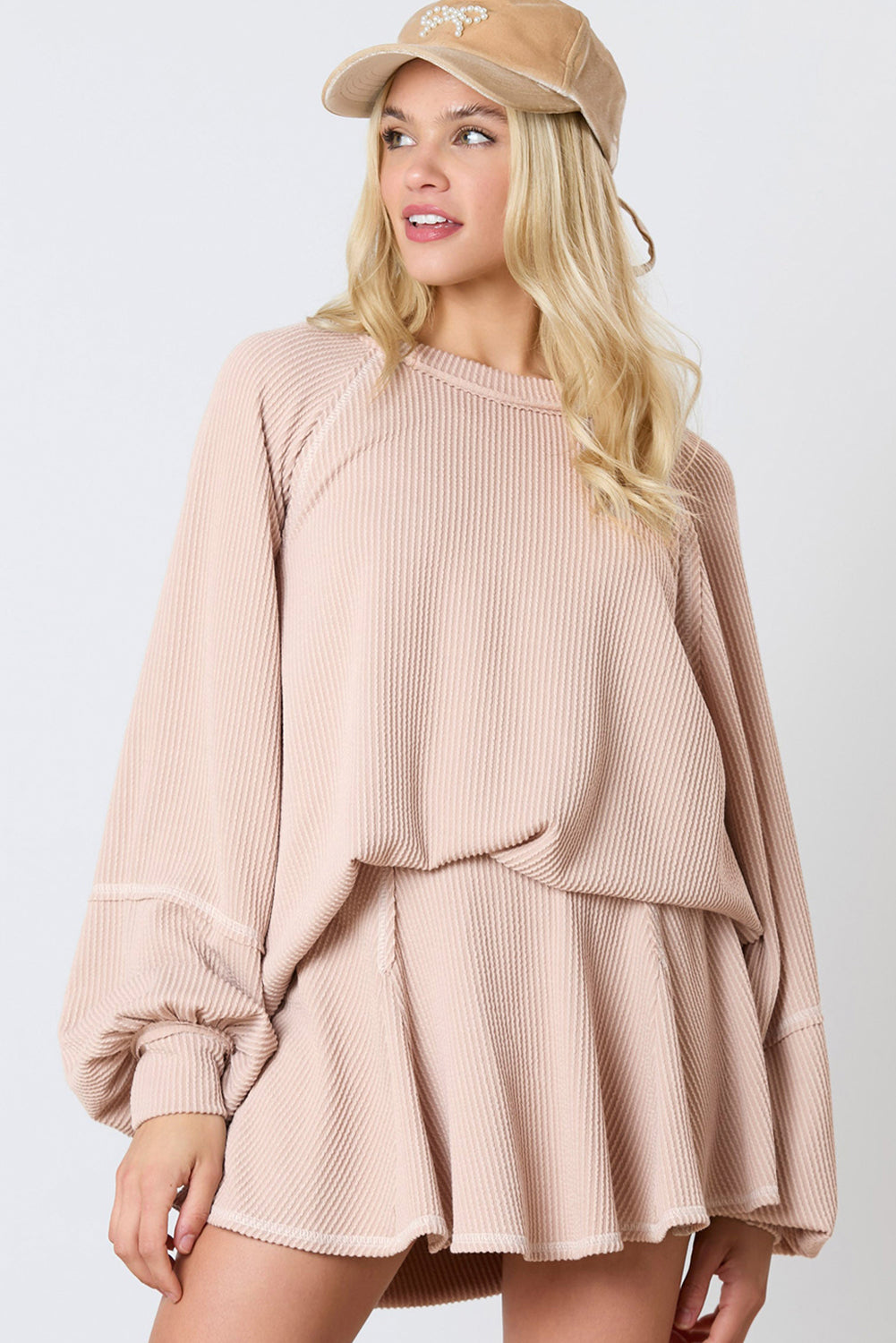 Woman wearing a beige ribbed sweater and skirt set with a matching cap on a white background