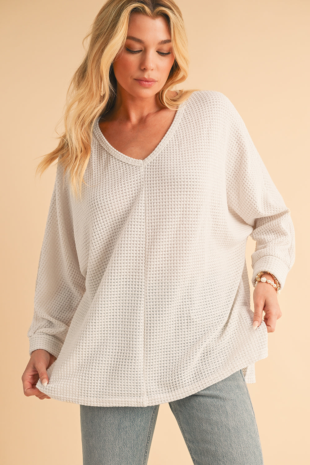 Woman wearing a beige textured sweater and gray pants on a beige background