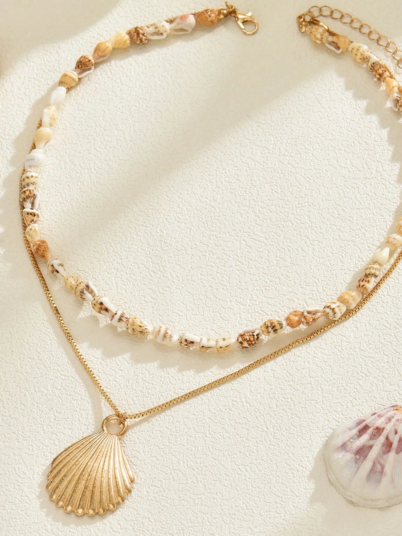 Necklace with shell pendant and beaded chain on a sandy background