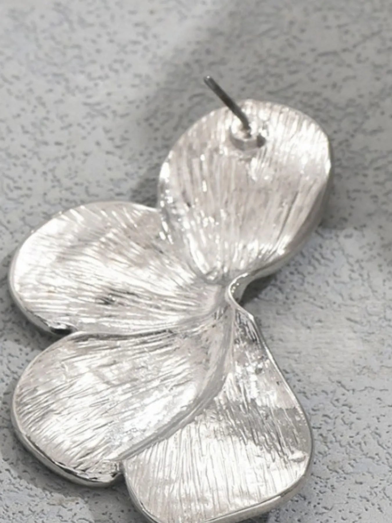 Silver leaf-shaped earring on a textured gray surface