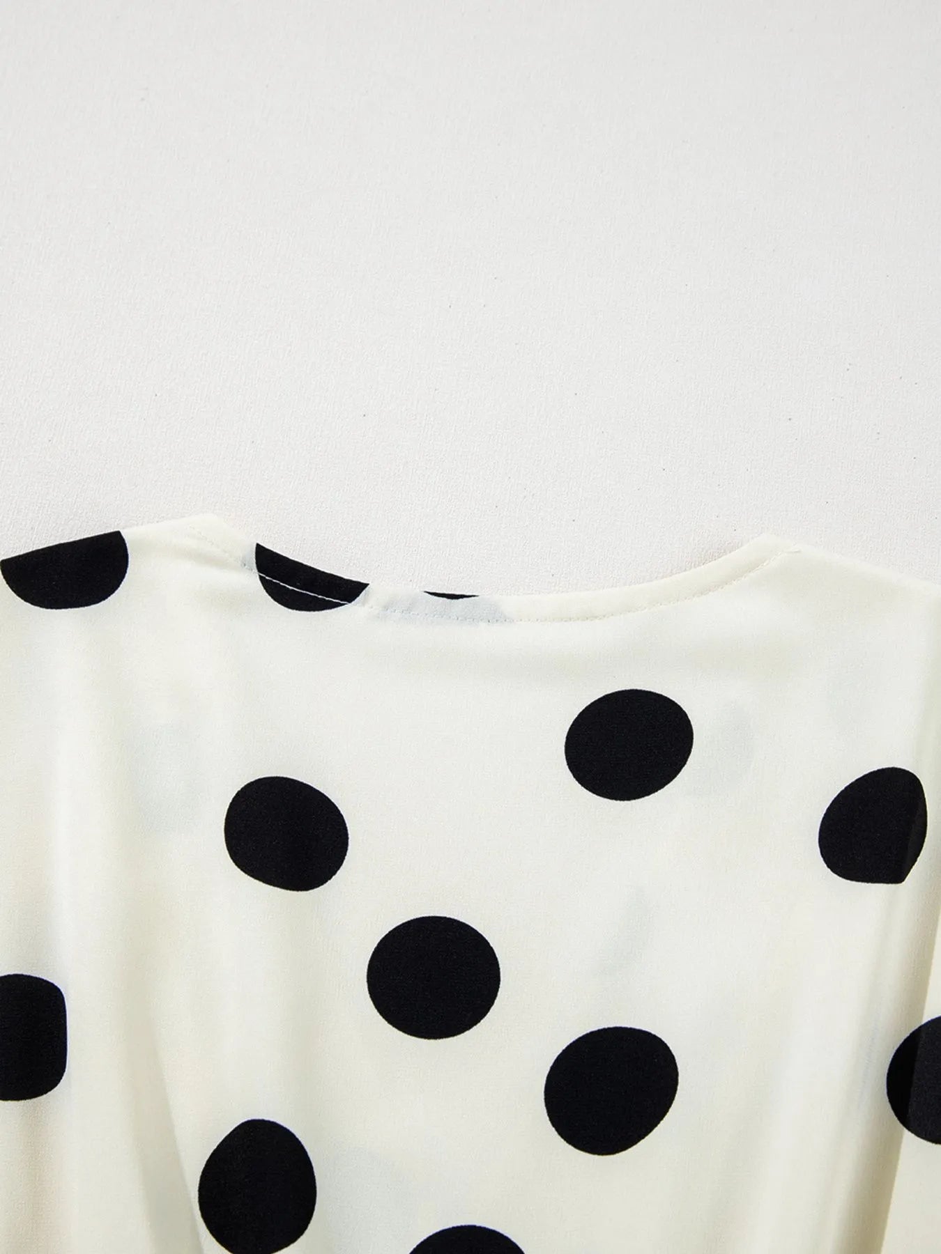 White top with black polka dots on a light gray background