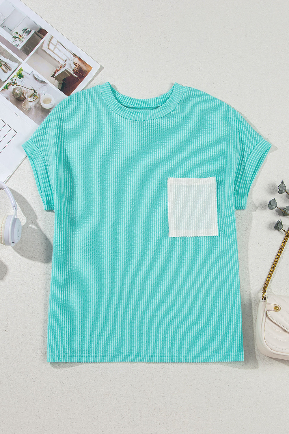 Teal t-shirt with a white pocket on a light gray surface