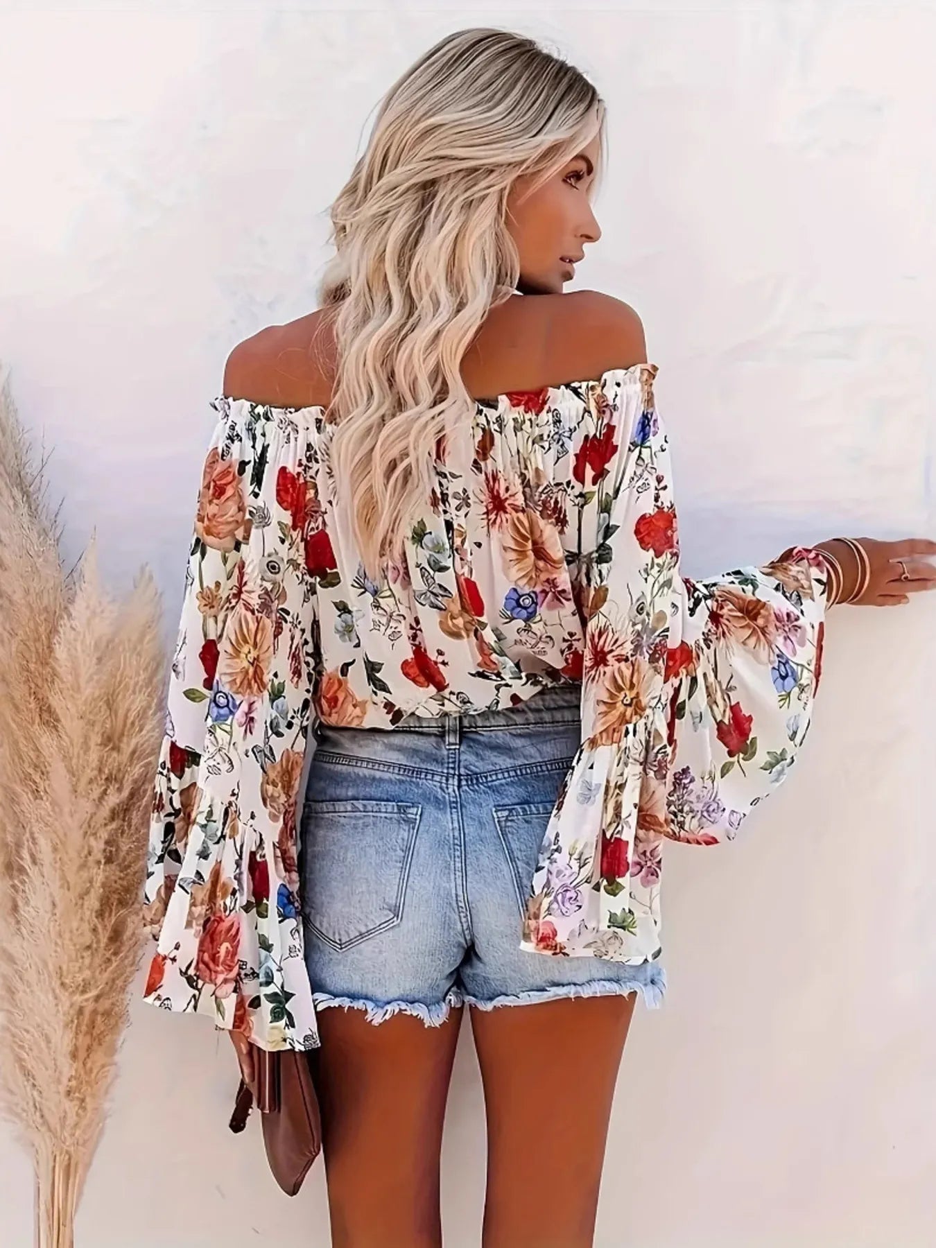 Woman wearing a floral off-shoulder top and denim shorts against a white background