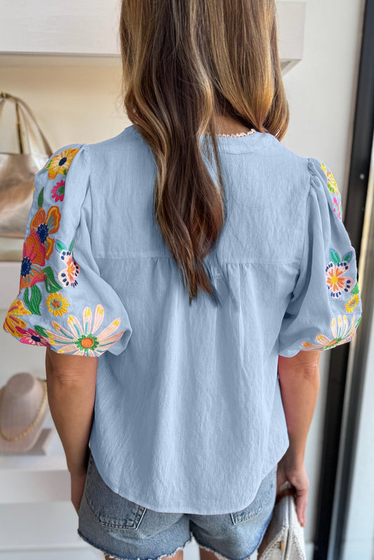 Light blue blouse with floral sleeves worn by a person indoors.