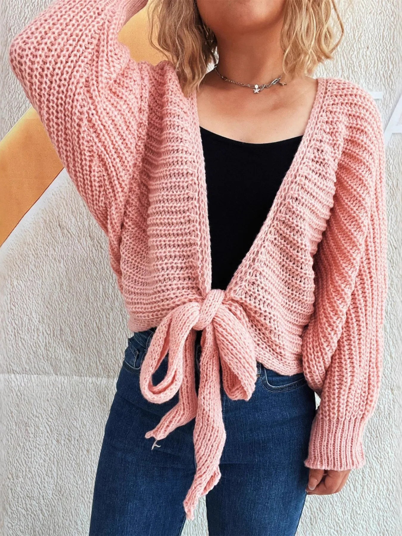 Person wearing a pink knitted cardigan over a black top and blue jeans against a light background