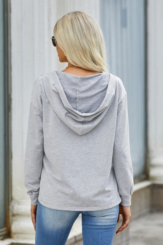 Person wearing a gray hoodie and blue jeans standing against a light-colored wall.