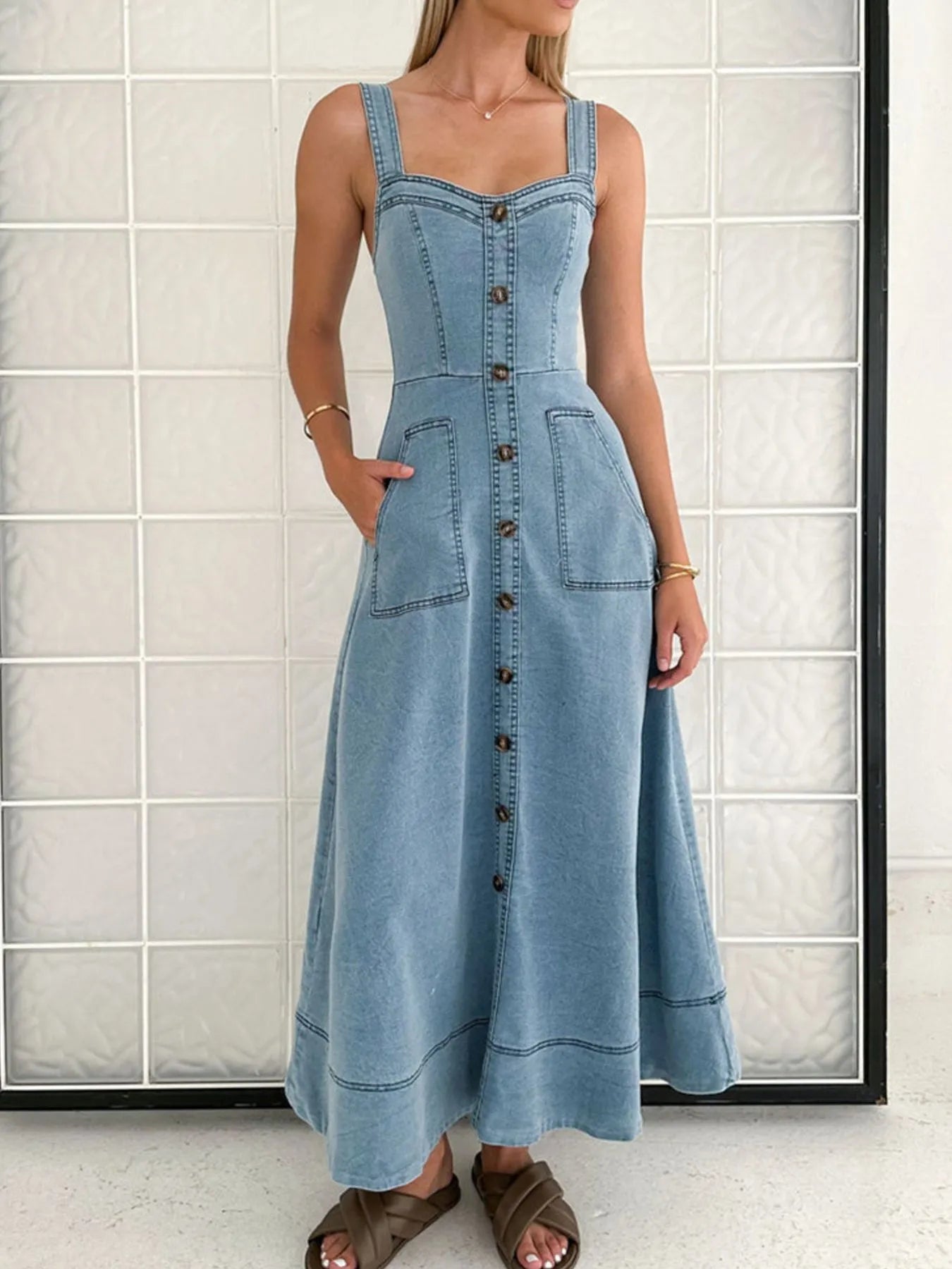 Woman wearing a blue denim dress with buttons against a tiled wall.
